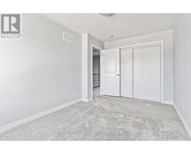 A white bedroom with a carpeted floor and a doorway leading to another room.