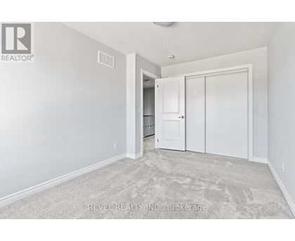 A white bedroom with a carpeted floor and a doorway leading to another room.