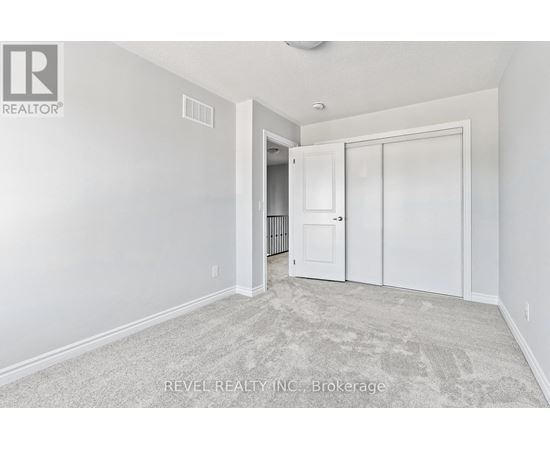 A white bedroom with a carpeted floor and a doorway leading to another room.