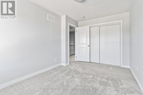 A white bedroom with a carpeted floor and a doorway leading to another room.