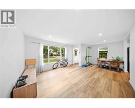 A spacious room with wooden flooring and a large window overlooking a garden.