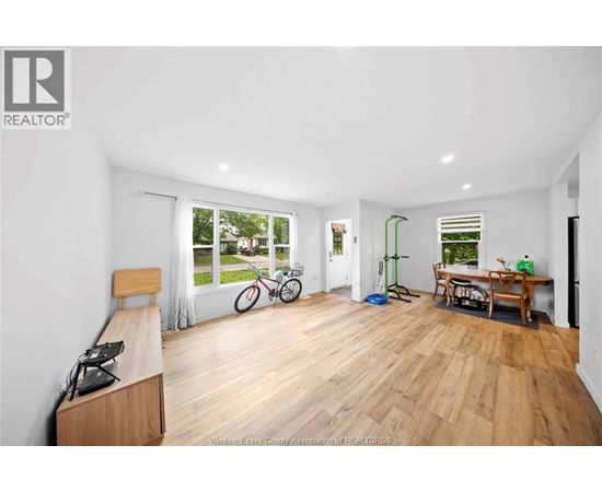 A spacious room with wooden flooring and a large window overlooking a garden.