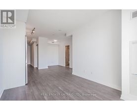 A spacious room with wood flooring and white walls, part of a real estate brokerage.