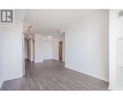 A spacious room with wood flooring and white walls, part of a real estate brokerage.