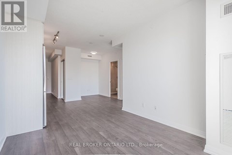 A spacious room with wood flooring and white walls, part of a real estate brokerage.