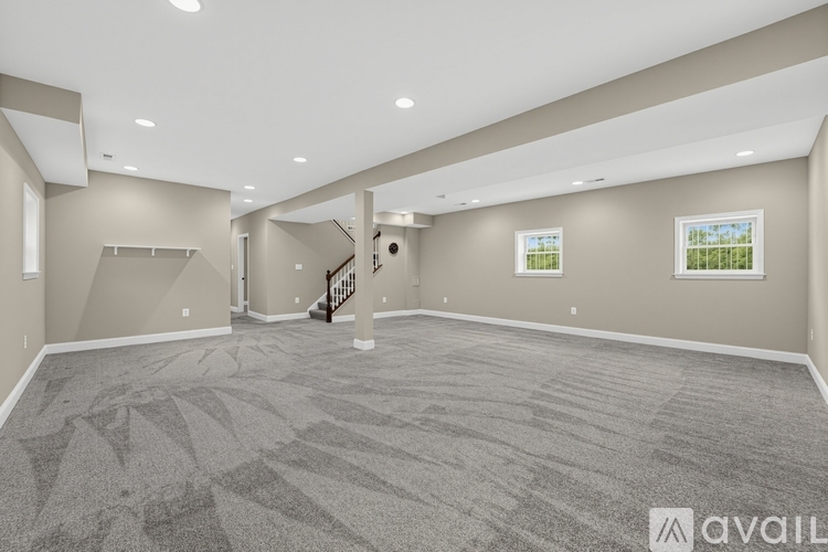 A spacious room with a carpeted floor and a staircase in the background.