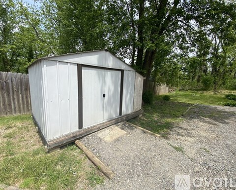 A white shed sits in a grassy area with trees in the background.