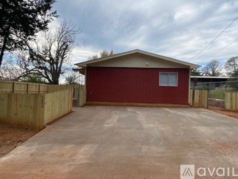 A red garage with a wooden fence and a concrete driveway.