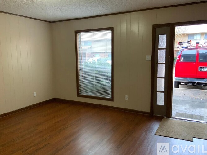 A room with wooden floors and a large window with a view of a parking lot.
