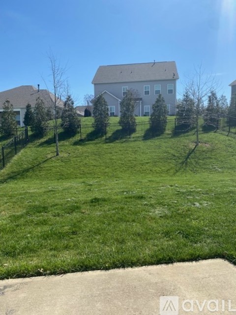 A white house with a grey roof is surrounded by a green lawn and trees.