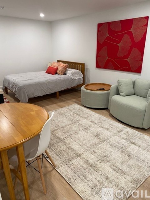 A bedroom with a bed, a couch, a table, and a painting on the wall.