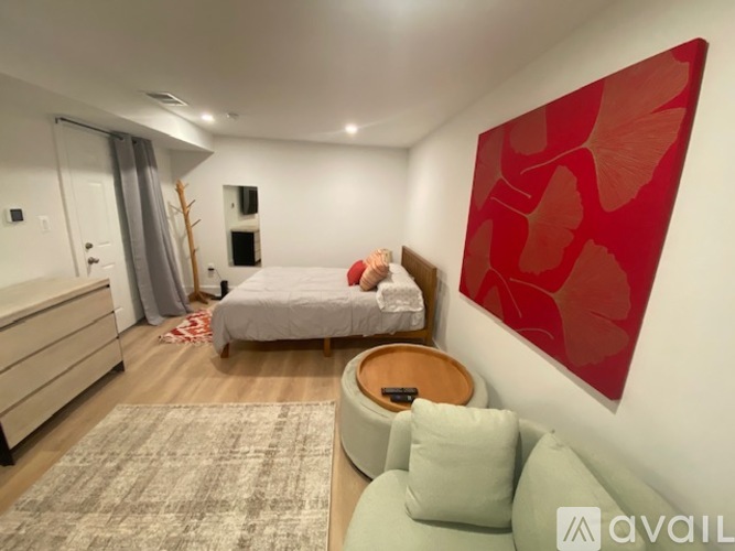 A bedroom with a bed, a chair, and a red leaf-patterned artwork on the wall.
