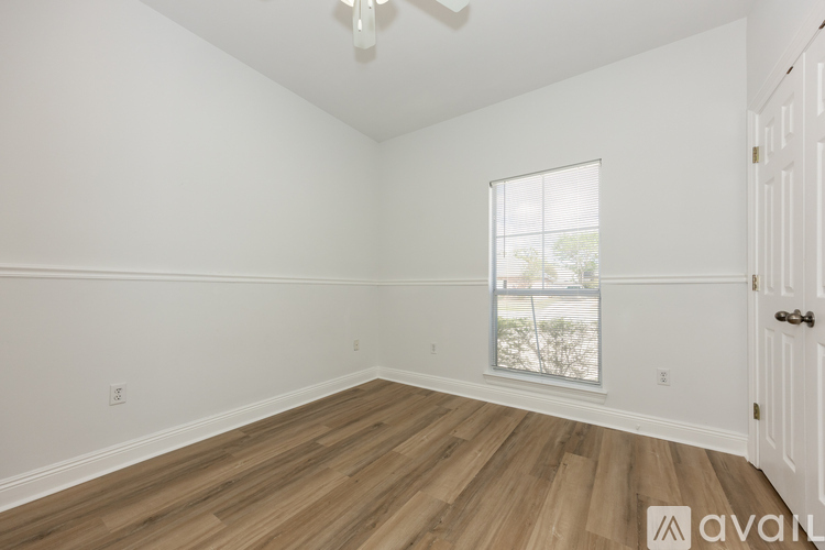A room with wooden floors and white walls, with a window showing a view of trees and a fence.