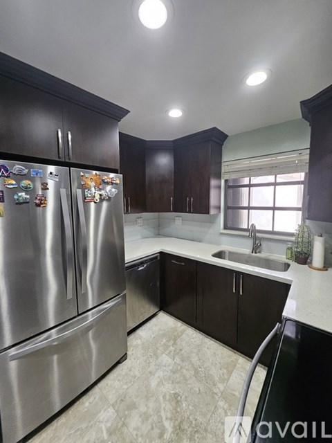 A kitchen with a stainless steel refrigerator and black cabinets.