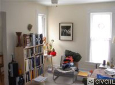A living room with a grey couch, a bookshelf filled with books, a small table with a lamp, and a framed picture on the wall.