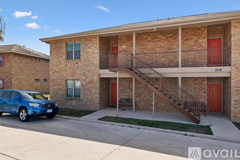 A blue car is parked in front of a brick building with a red door.