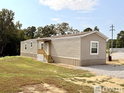 A mobile home with a brown siding and a white door is surrounded by a grassy area.
