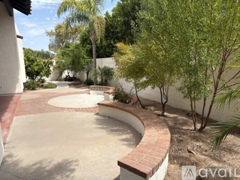 A backyard with a brick pool and a white wall.