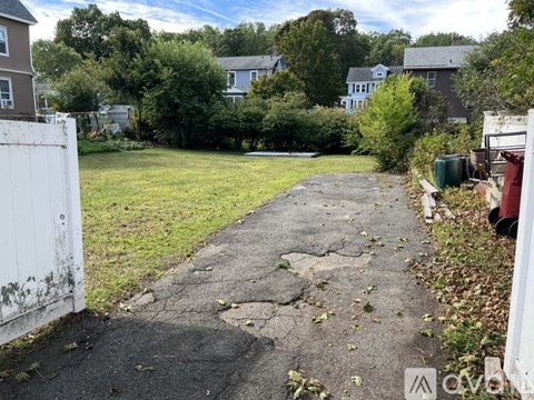 A white fence borders a patch of grass and a cracked concrete path.