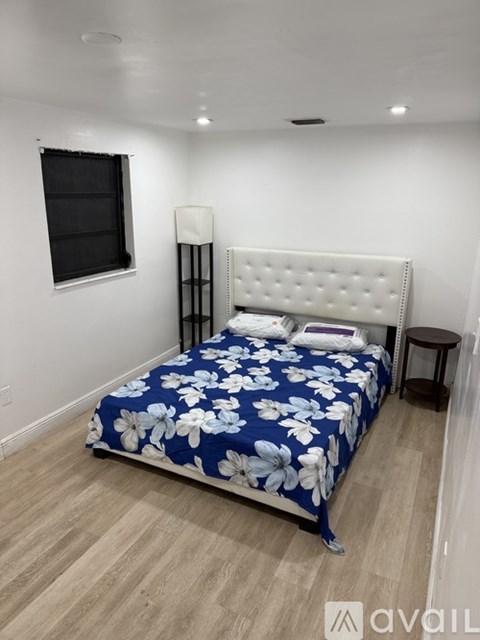 A bedroom with a bed, nightstand, and a window.
