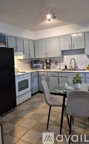 A kitchen with a black refrigerator, white cabinets, and a glass table with two chairs.
