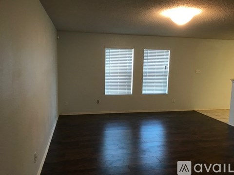A room with wooden floors and two windows with blinds.