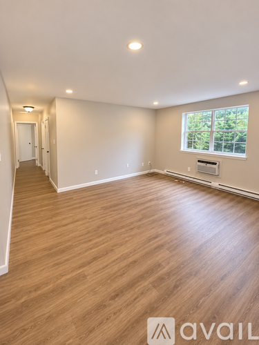 A spacious room with wooden flooring and a window overlooking greenery.