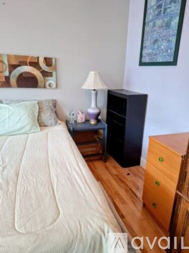 A bedroom with a bed, nightstand, and a painting on the wall.