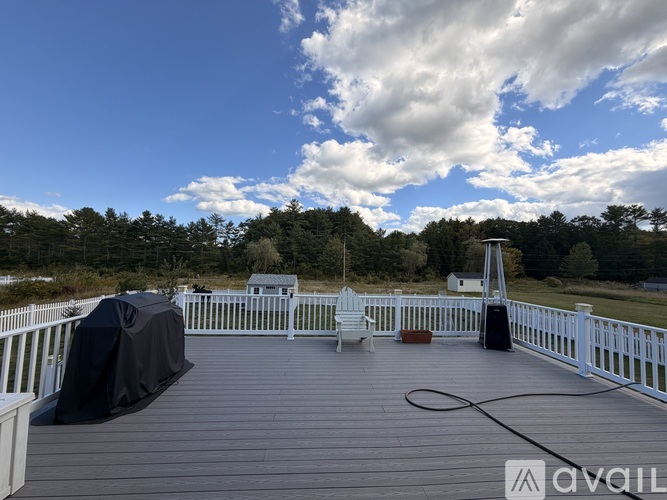A deck with a white railing and a black cover is set against a backdrop of trees.