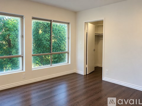 A room with wooden floors and a large window with a view of trees.