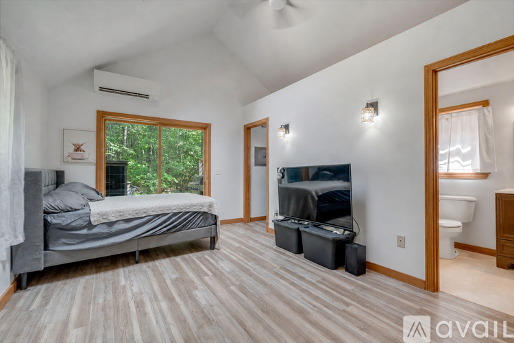 A bedroom with a bed, a television, and a window with a view of trees.