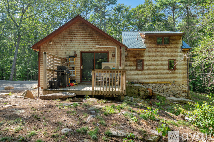 A wooden cabin with a porch and a green roof is surrounded by trees.