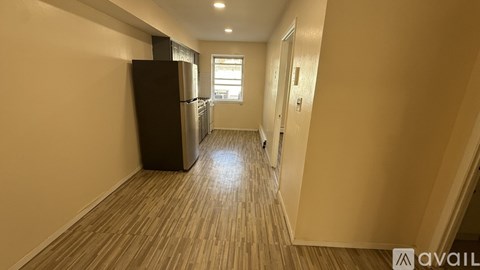 A long hallway with a black refrigerator on the left and a door on the right.