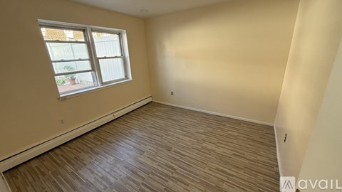A room with wooden flooring and a window overlooking a building.