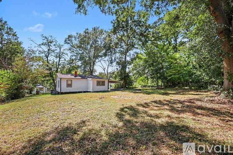 A small white house is surrounded by trees and grass.