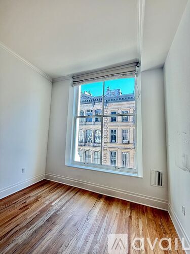 A room with wooden floors and a window showing a building outside.