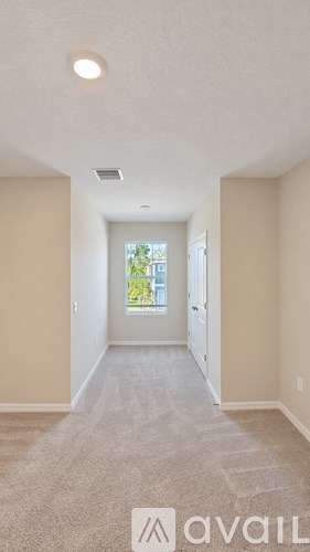 A hallway with a carpeted floor and a window with a view of trees and a building outside.