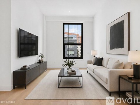 A living room with a large window, a couch, a coffee table, and a TV mounted on the wall.