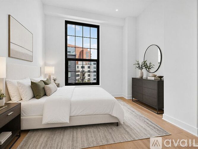 A bedroom with a large bed, a window with a view of buildings, and a grey rug on the floor.