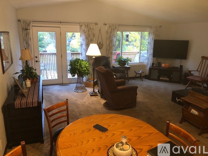 A living room with a wooden table and chairs, a couch, a television, and a potted plant.