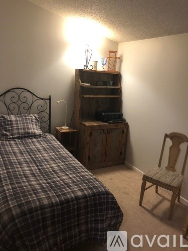 A bedroom with a bed, chair, and a shelf with a lamp on it.