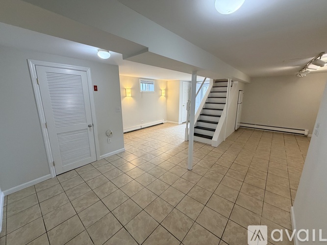 A spacious room with tiled flooring and a staircase leading to another level.