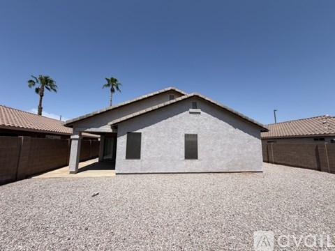 A house with a grey roof and a brown fence with two palm trees in the background.