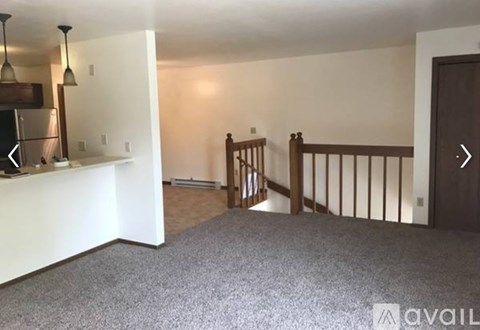A living room with a carpeted floor and a wooden staircase.