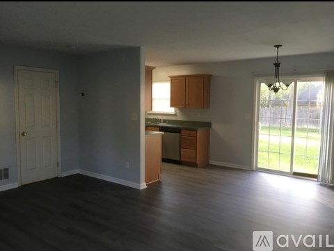 A room with wooden floors and a kitchen area with cabinets and a counter.