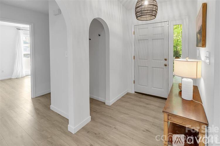 A room with a white door, a wooden table with a lamp on it, and a white wall with a hanging light fixture.