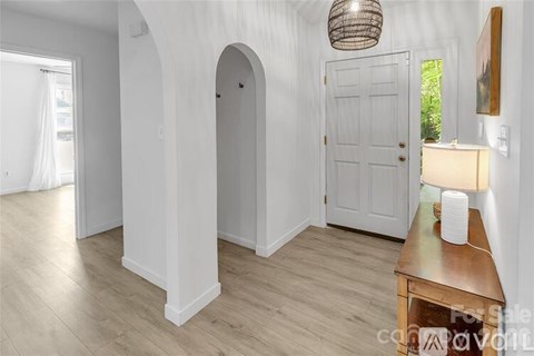 A room with a white door, a wooden table with a lamp on it, and a white wall with a hanging light fixture.