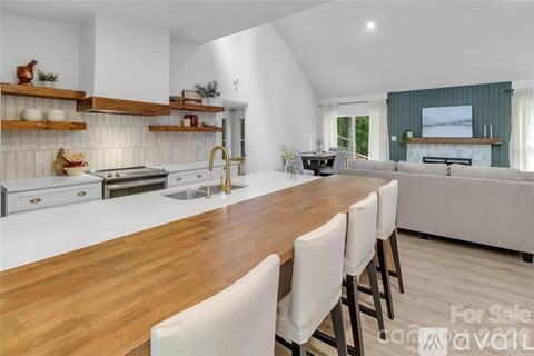 A kitchen with a long wooden table and white chairs is for sale.