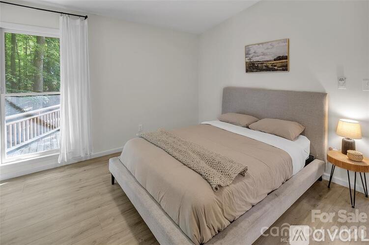 A bedroom with a large bed and a view of a deck outside the window.