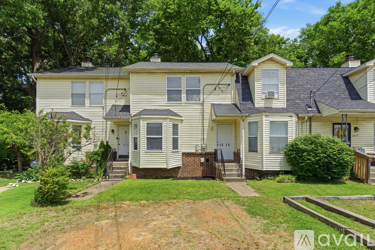 A two-story house with a front yard and a tree in the background.